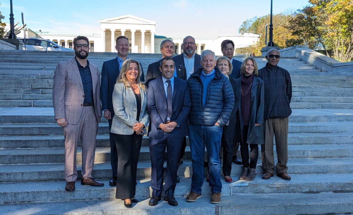 Photo of a group of 11 individuals standing to pose for the camera by the grand staircase in Delaware Park