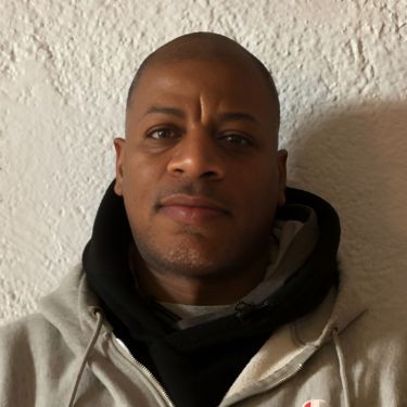 Kinny wearing a grey sweatshirt and black hoodie against a beige wall