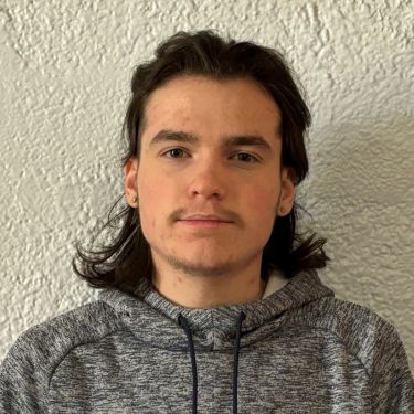 Male with black shoulder length hair wearing a grey hoodie sweatshirt